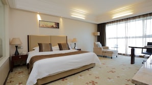 A hotel room with a large bed, two bedside tables with lamps, a desk, a chair, and a large window with curtains. - Arcadia International Hotel (Langfang)