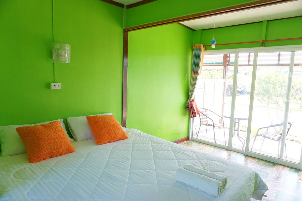A room with a bed, green walls, a window with a view, and a power outlet.