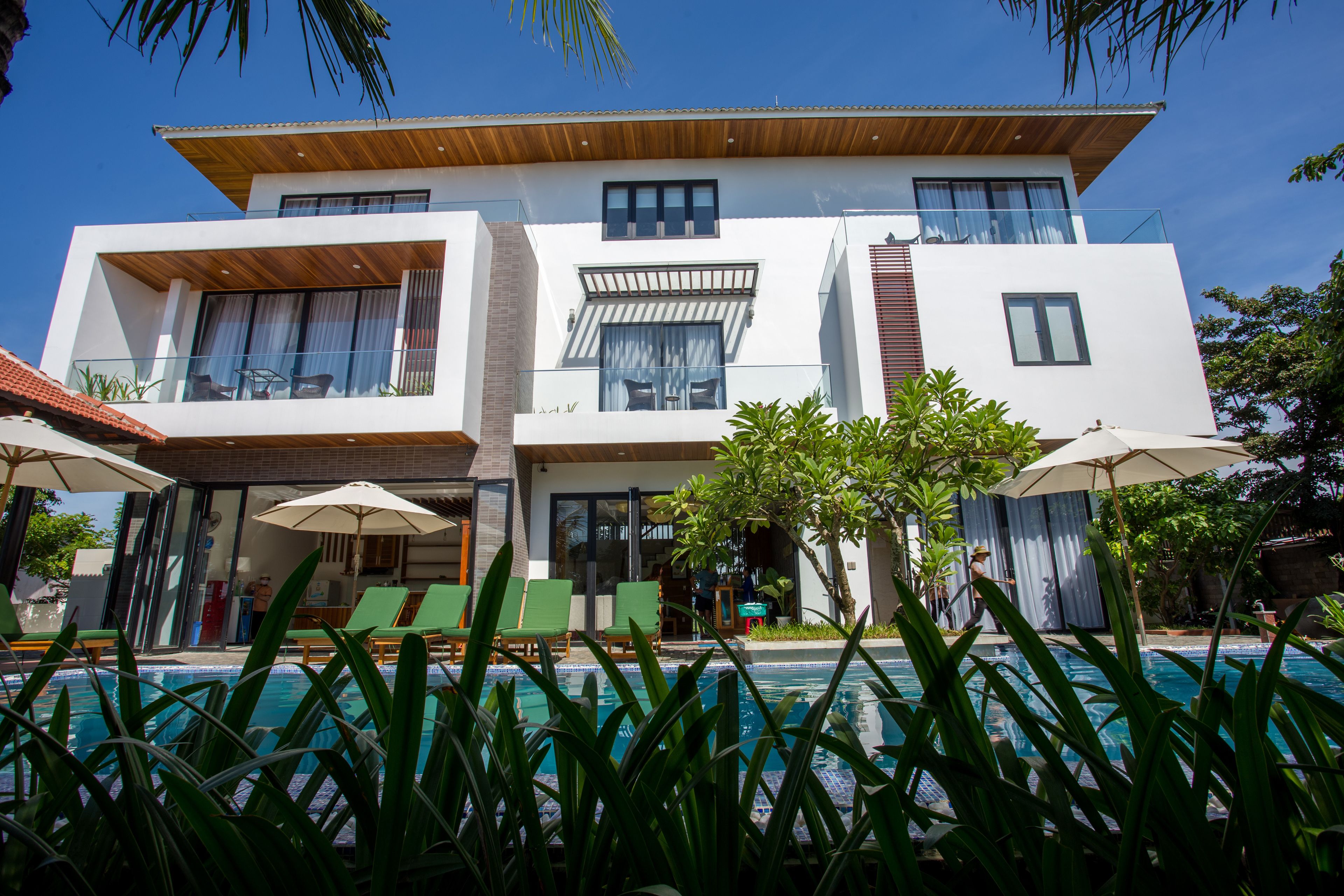 A modern two-story house with a swimming pool, outdoor seating, and lush greenery.