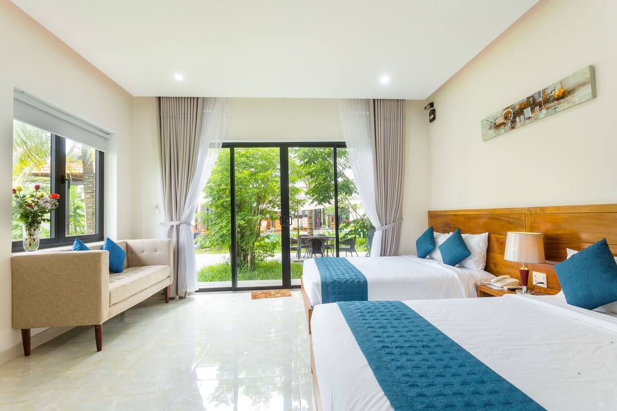 Une chambre d’hôtel avec deux lits, un canapé, une table à manger et une vue sur la verdure.