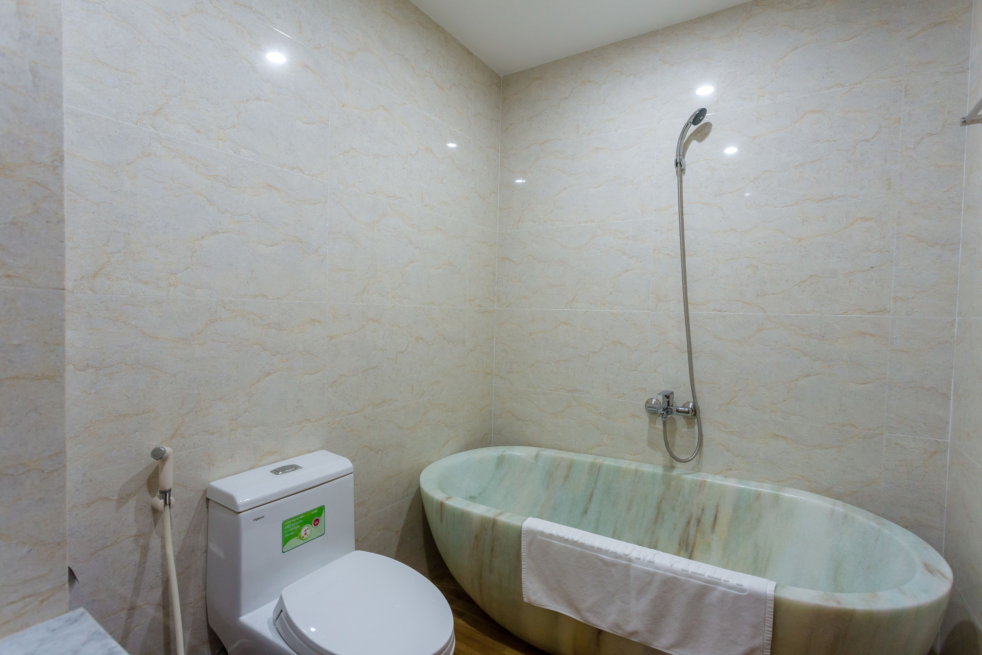 A bathroom with a marble wall, a toilet, and a freestanding bathtub with a showerhead.
