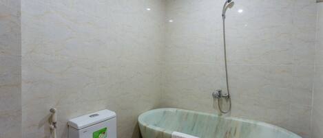 A bathroom with a marble wall, a toilet, and a freestanding bathtub with a showerhead.