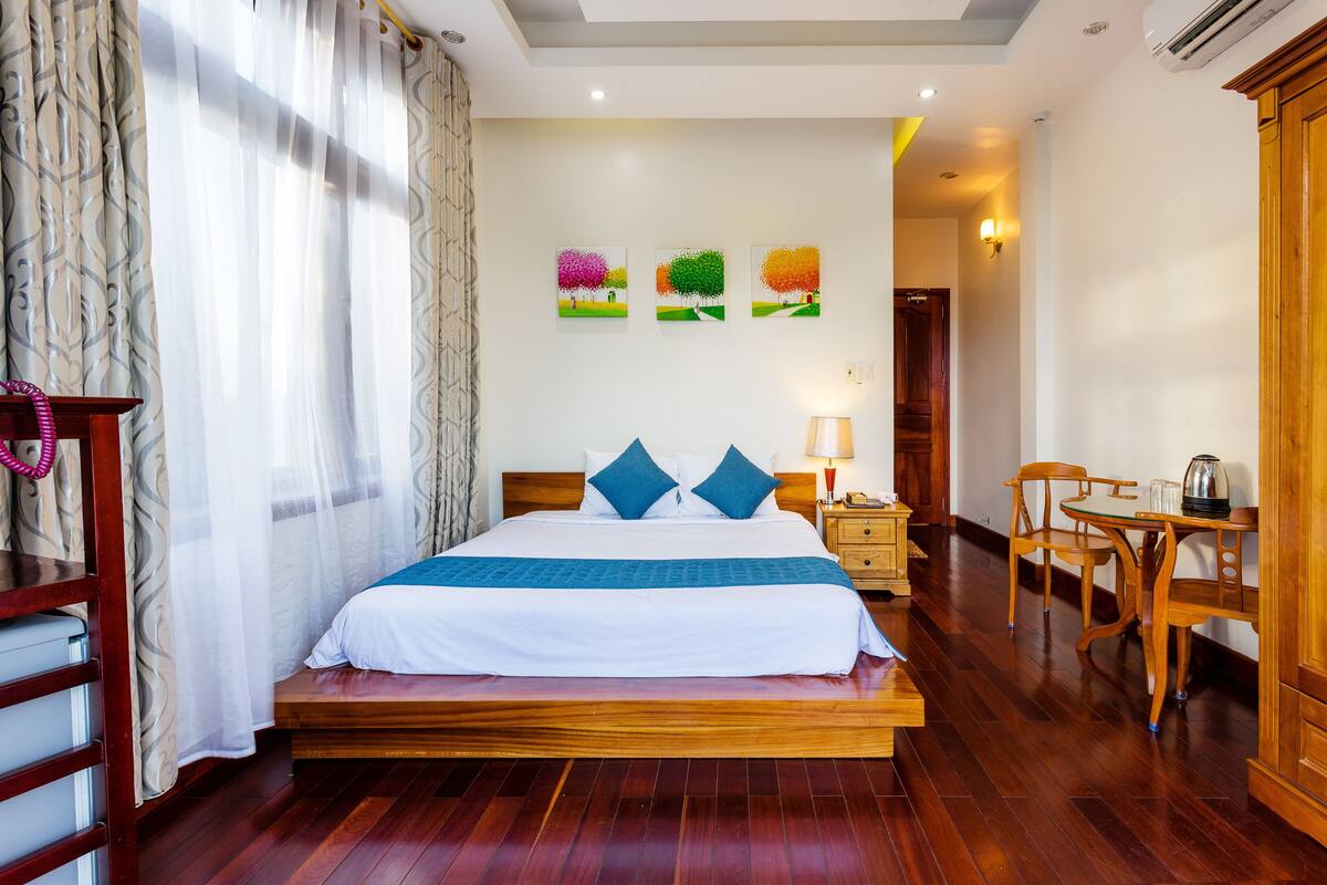 Une chambre d’hôtel avec un lit en bois, un bureau avec une chaise, une lampe et des œuvres d’art murales représentant des arbres.