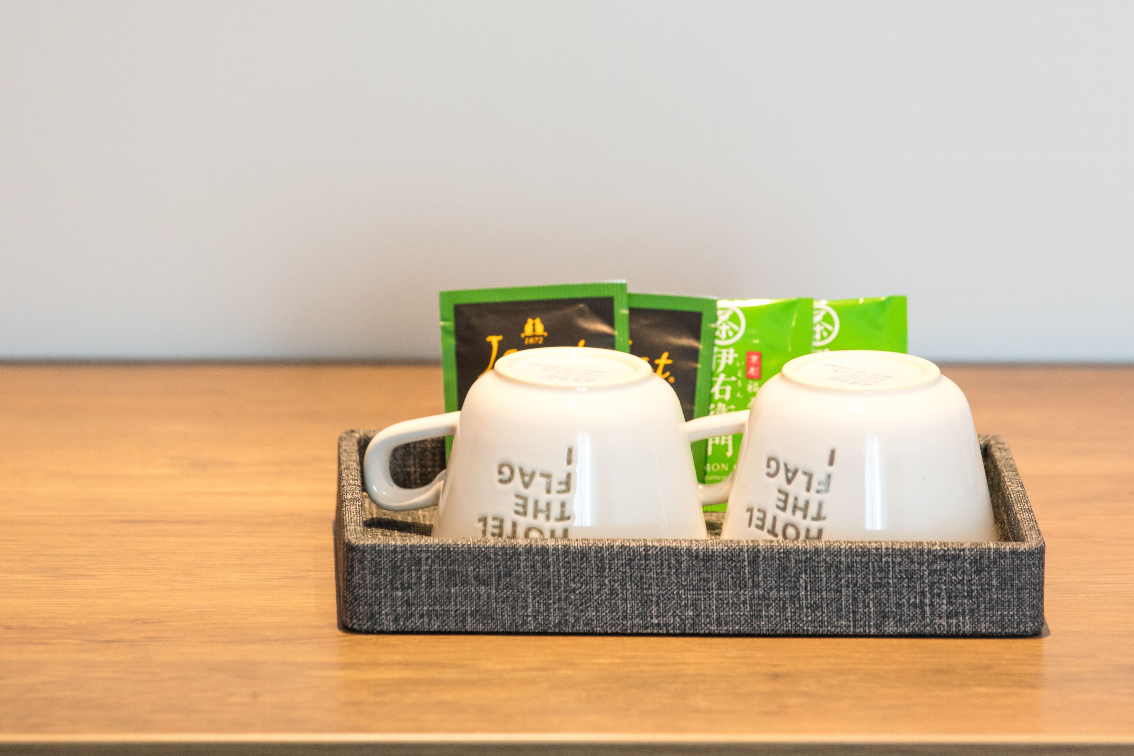 Two white ceramic mugs with text on them, placed in a woven basket on a wooden surface.