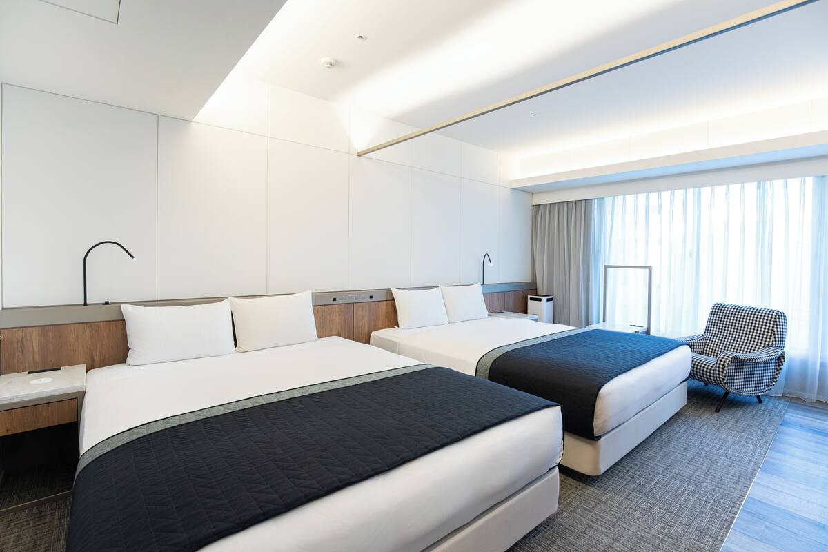 A hotel room with two beds, a desk, a chair, and a large window with curtains.