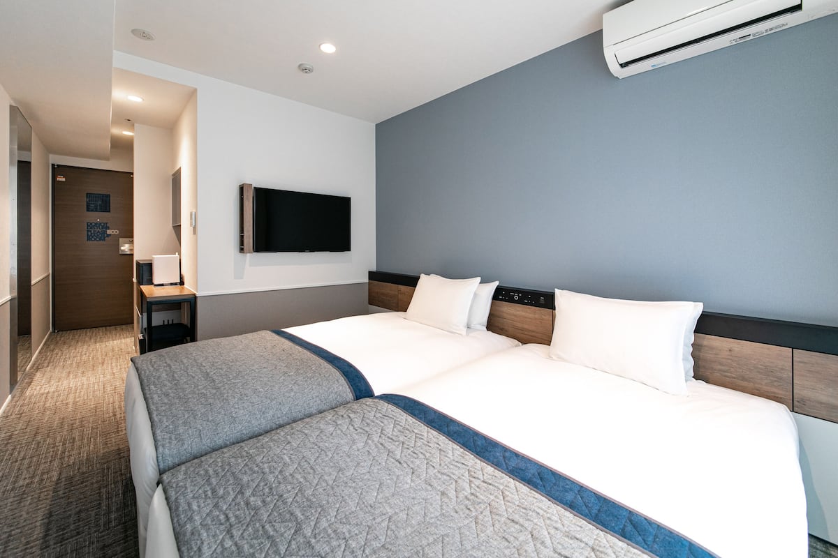 A hotel room with a large bed, a flat-screen TV mounted on the wall, and an air conditioning unit above the bed.