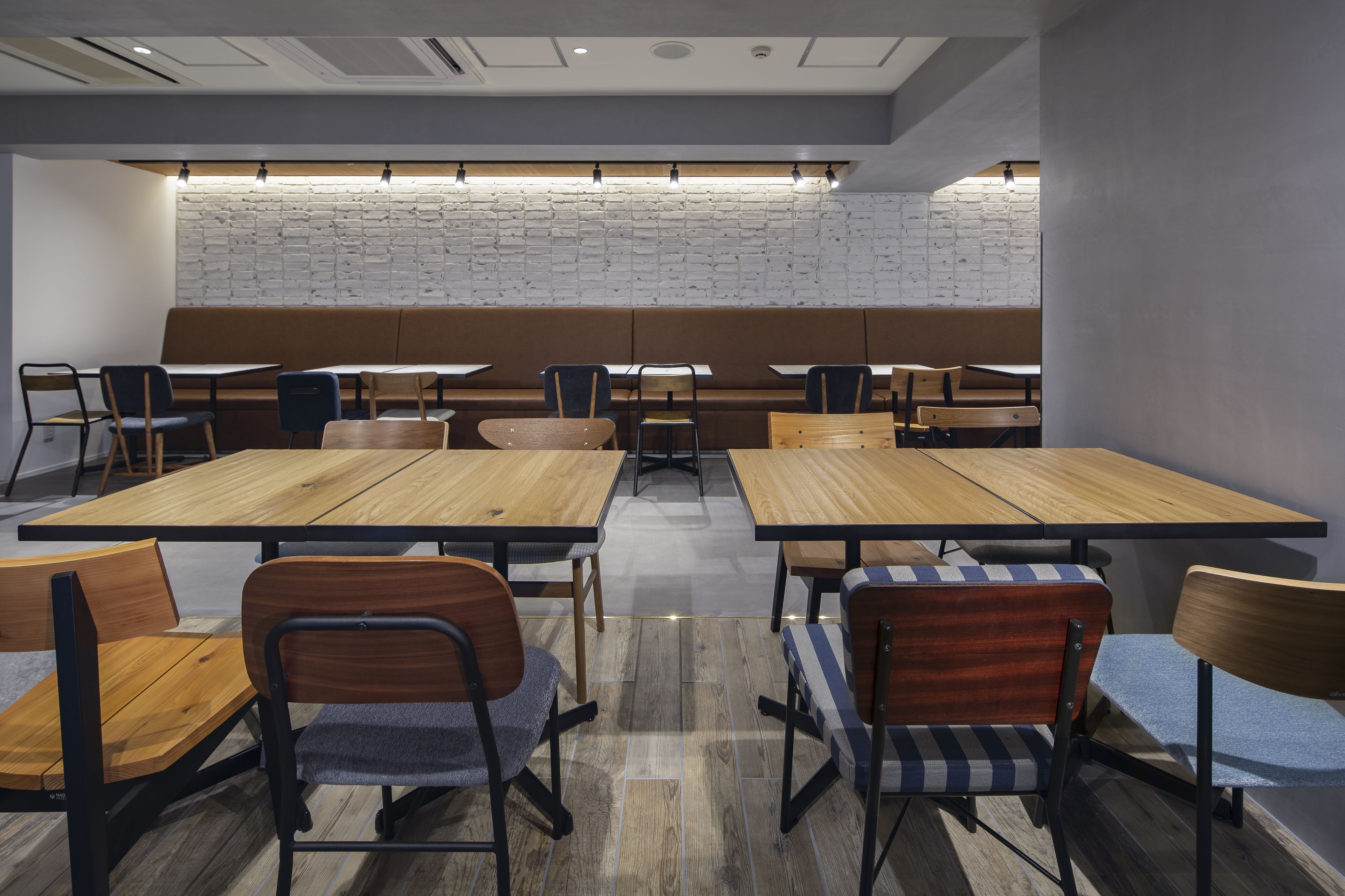 A modern dining area with wooden tables and chairs, a brick wall, and recessed lighting.