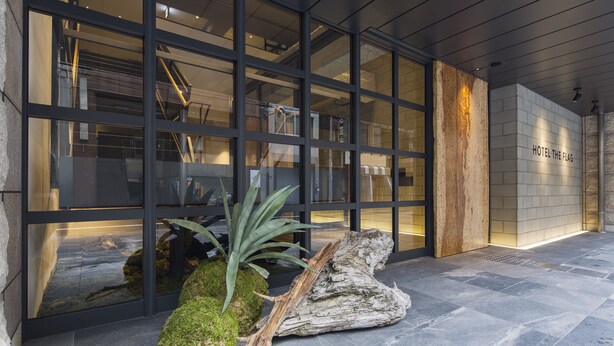 A modern hotel entrance with large glass windows, a stone wall with the hotel name, and a stone floor.