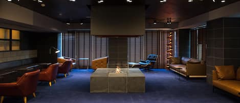 Un espace de détente moderne doté d’un foyer central, de différents types de sièges et d’un grand luminaire au plafond.