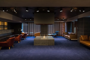 Un espace de détente moderne doté d’un foyer central, de différents types de sièges et d’un grand luminaire au plafond.