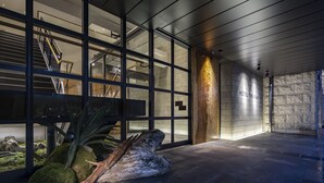 A modern hotel lobby with a glass facade, a staircase, and a stone wall with the hotel's name.