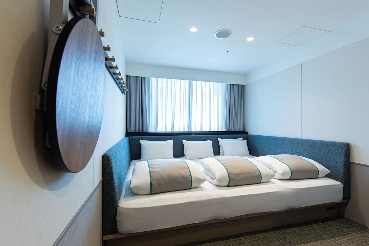 A hotel room with a bed, a large mirror, a window with curtains, and a ceiling with recessed lighting.