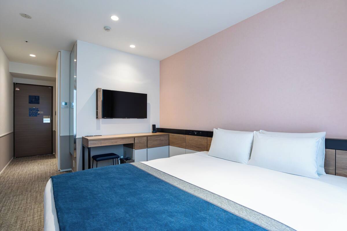 A hotel room with a bed, a desk, a chair, a television, and a door.
