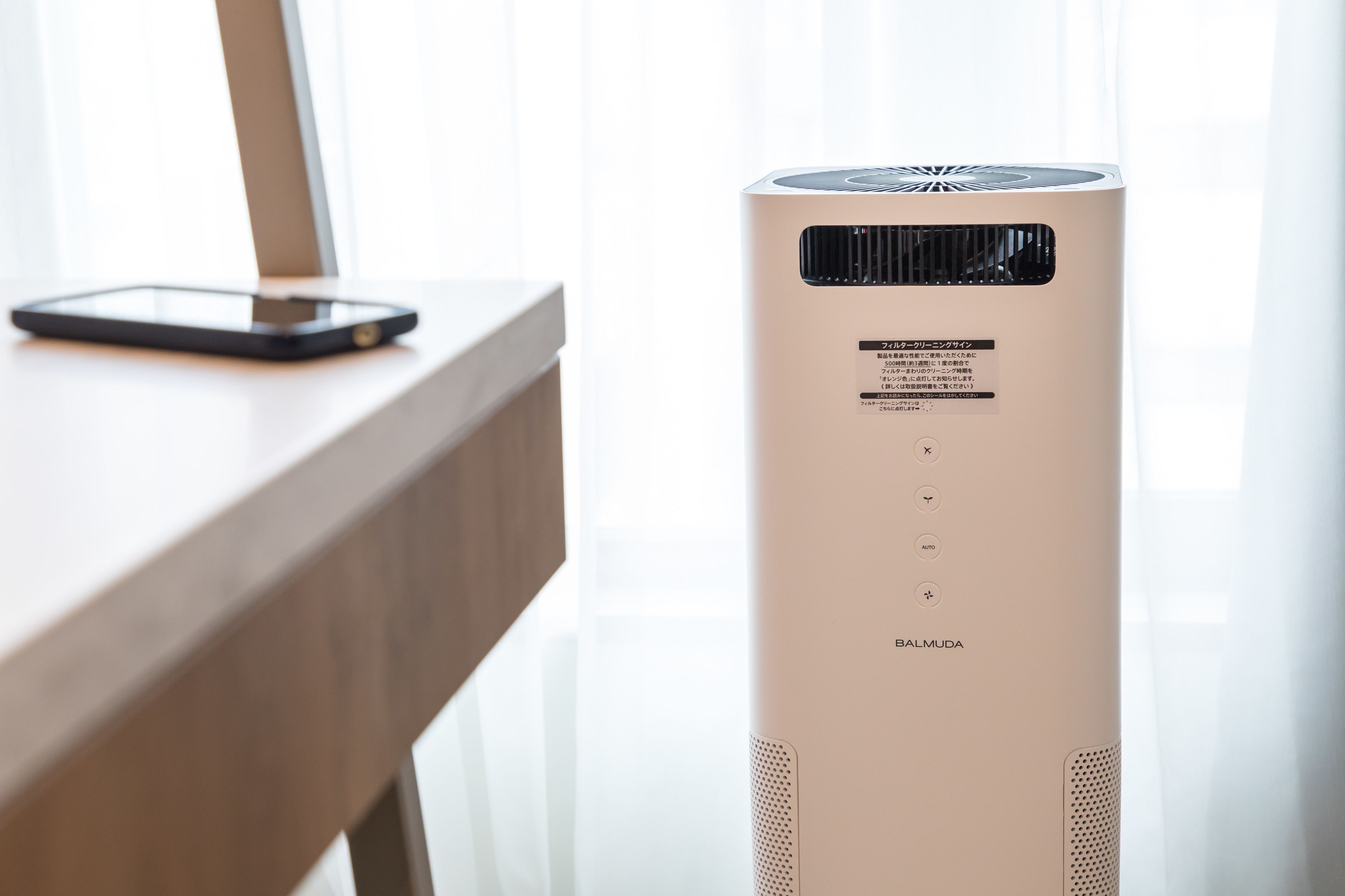 A tall, beige-colored air purifier with a control panel and a smartphone on a wooden surface.