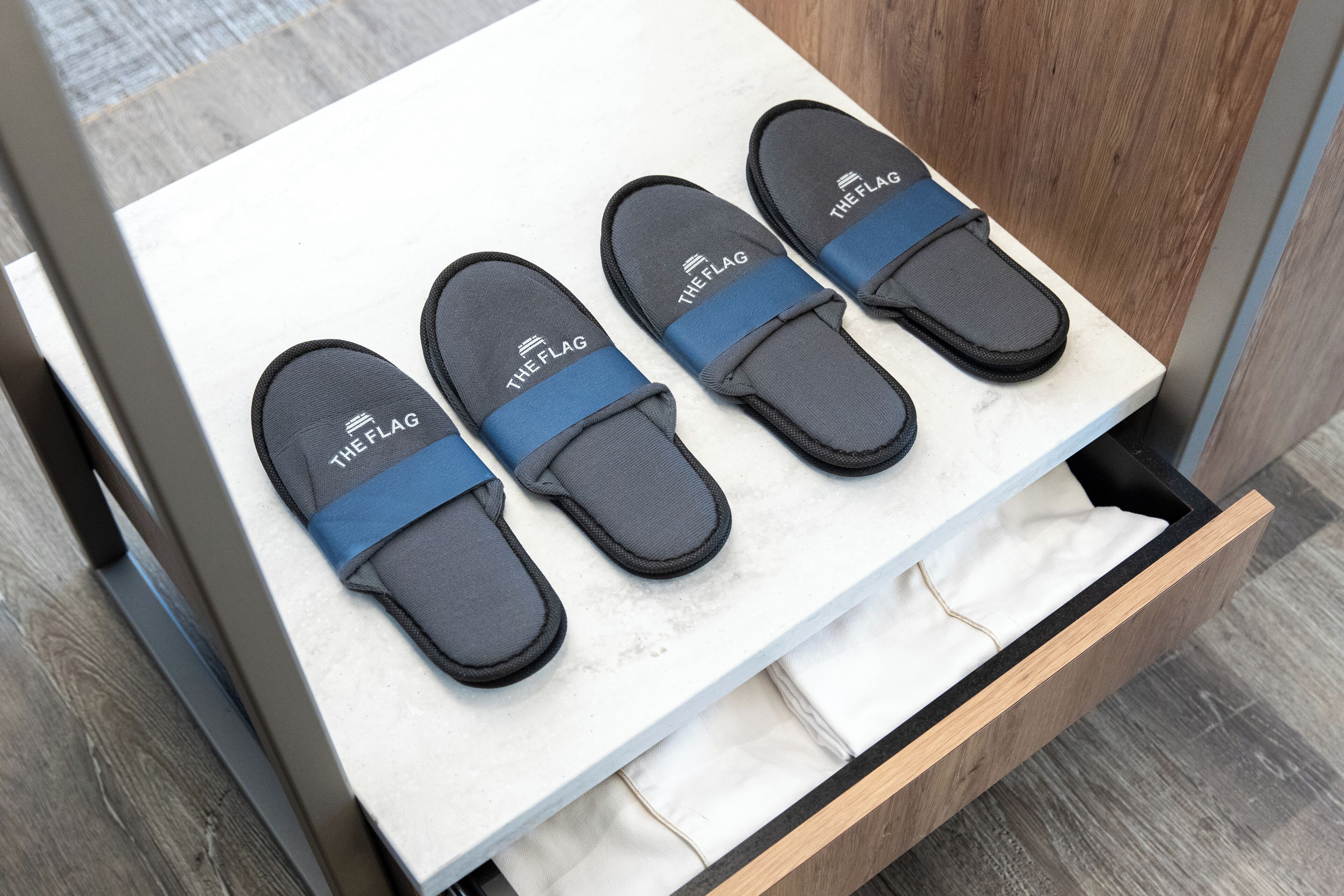 Un cajón con tres pares de pantuflas negras con correas azules etiquetadas como "THE FLAG".