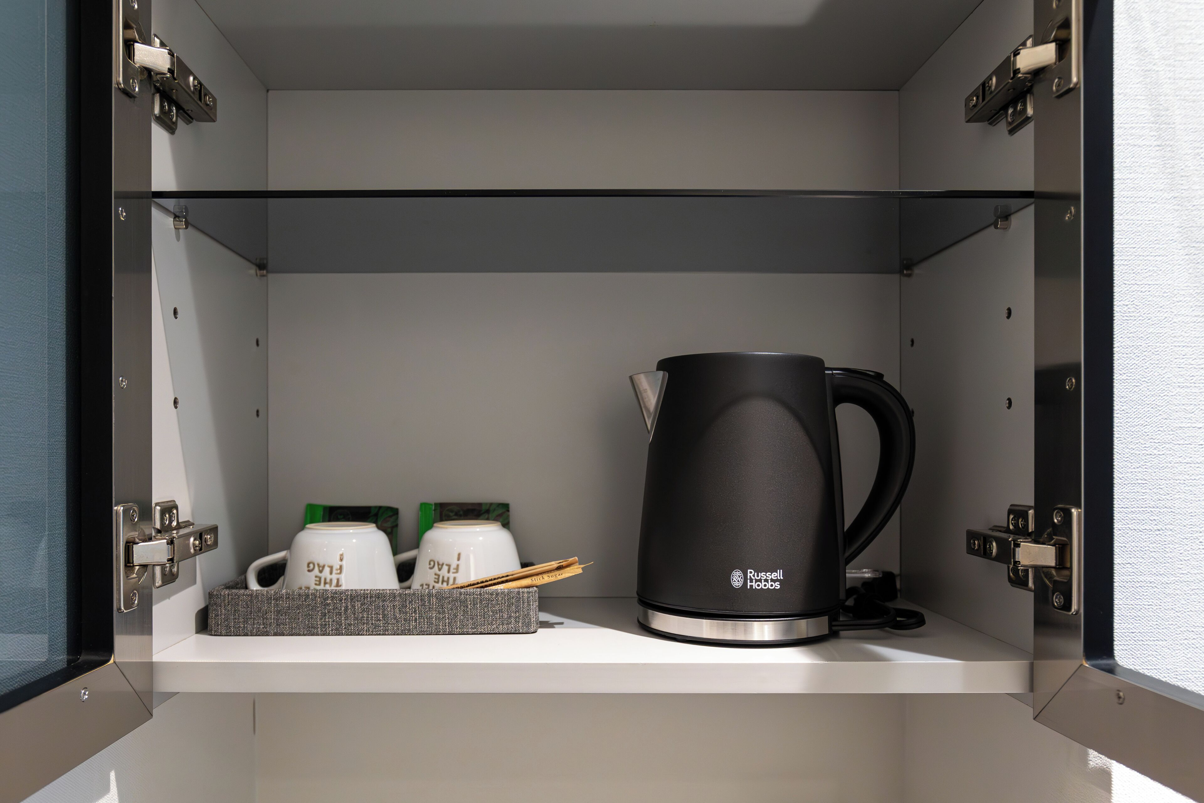 A compact kitchenette with a black Russell Hobbs coffee maker, a white mug, and a small tray with utensils.