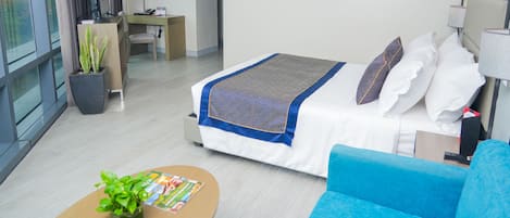 Habitación de hotel con cama, escritorio, silla, sofá azul y planta en maceta.