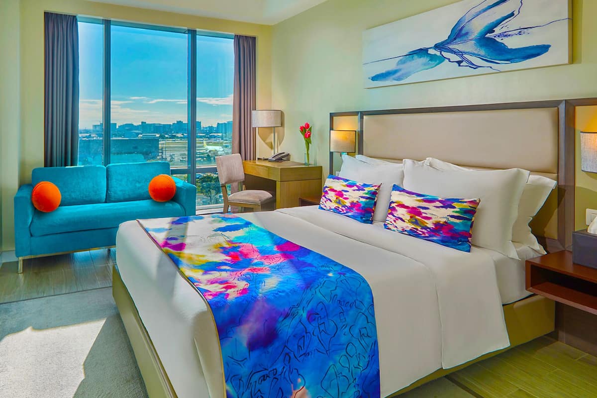 A hotel room with a large bed, a sofa, a desk, and a view of the city.
