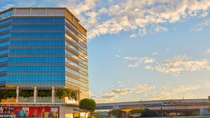 Un hotel moderno con fachada de vidrio, cerca de un puente y una vía de tren.