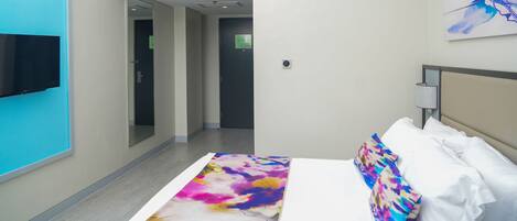 Habitación de hotel con una cama, un televisor montado en la pared, una puerta y un cuadro.