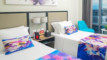 A hotel room with two beds, a small table with a plant, and a window with a city view.