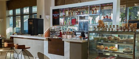Un espace bar avec un comptoir, des tabourets et une vitrine où sont exposées des pâtisseries.