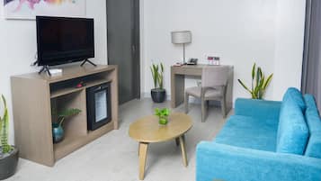 A modern living room with a flat-screen TV, a desk with a lamp, a blue sofa, and potted plants.