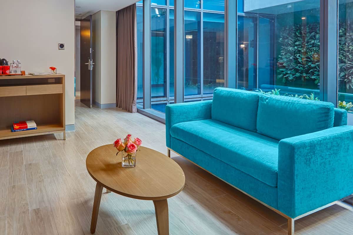 A modern hotel lobby with a wooden reception desk, a teal sofa, and a small round table with a vase of flowers.