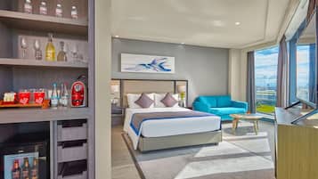 A modern hotel room with a bed, a blue sofa, a coffee table, and a minibar.