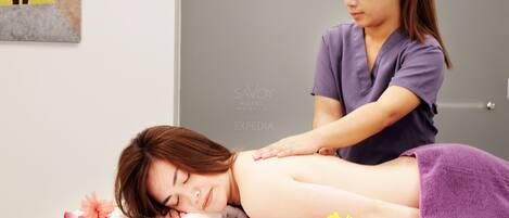 A massage therapy session in a spa setting with a client lying on a massage table, a therapist attending to the client, and scattered rose petals on the table.