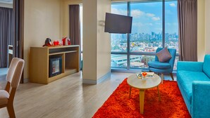 Un salón moderno con vista a la ciudad, un televisor de pantalla plana, un sofá color esmeralda, un tapete rojo y una mesa de centro de madera.