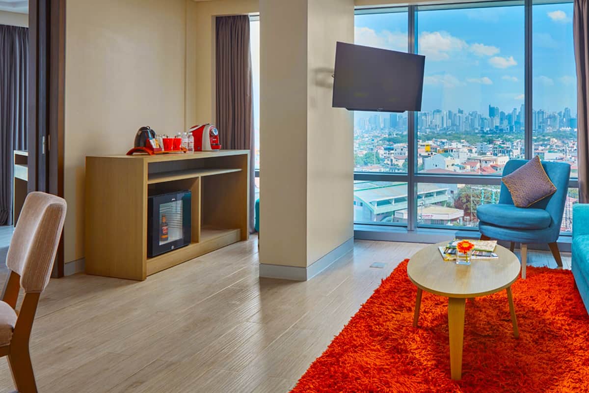 A modern living room with a city view, a flat-screen TV, a teal sofa, a red rug, and a wooden coffee table.