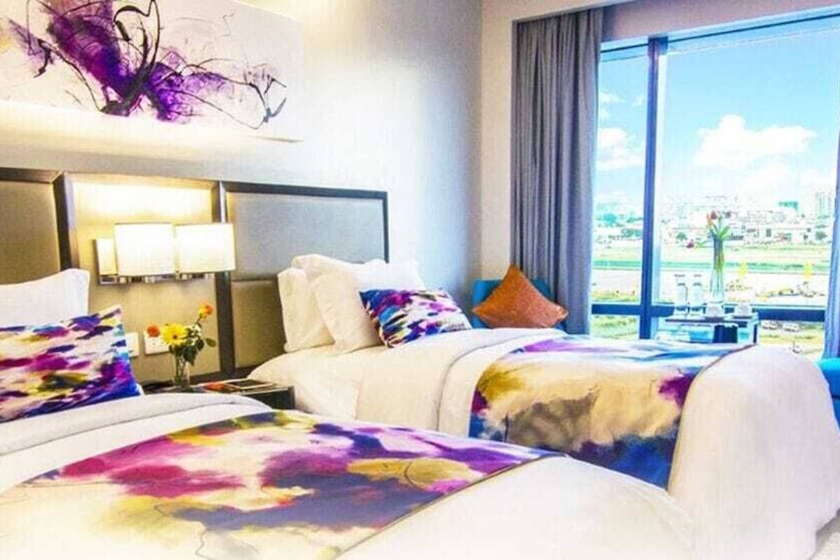 A hotel room with two beds, a sofa, a large window with a view, and a painting on the wall.