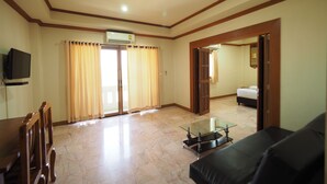 A living room with a glass coffee table, a sofa, a TV mounted on the wall, and a sliding door leading to a bedroom. - Amorn Sukhothai Hotel (Sukhothai)