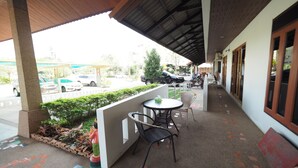 A covered outdoor seating area with a table and chairs, a small garden, and a view of the street. - Amorn Sukhothai Hotel (Sukhothai)