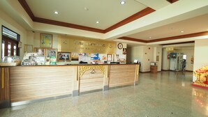 A reception area with a wooden reception desk, framed pictures, and a clock on the wall. - Amorn Sukhothai Hotel (Sukhothai)