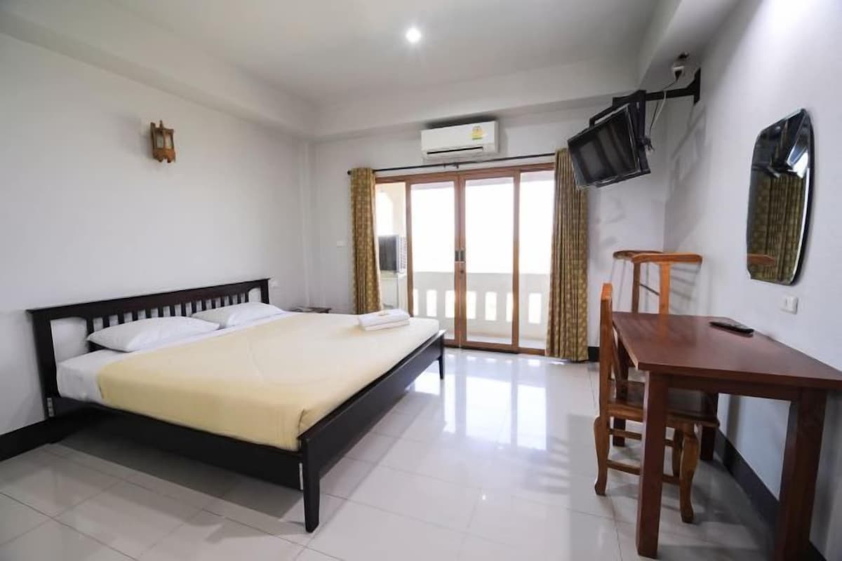 Habitación de hotel con cama, escritorio, silla, televisor montado en la pared y puerta corrediza de vidrio que da a un balcón.