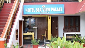A hotel entrance with a reception desk, a staircase, and potted plants.