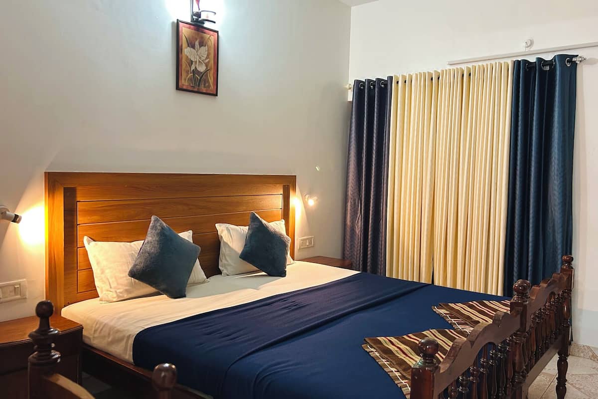 A neatly made bed with a wooden headboard, two pillows, and a blue bedspread. There is a nightstand with a lamp and a wall-mounted picture.