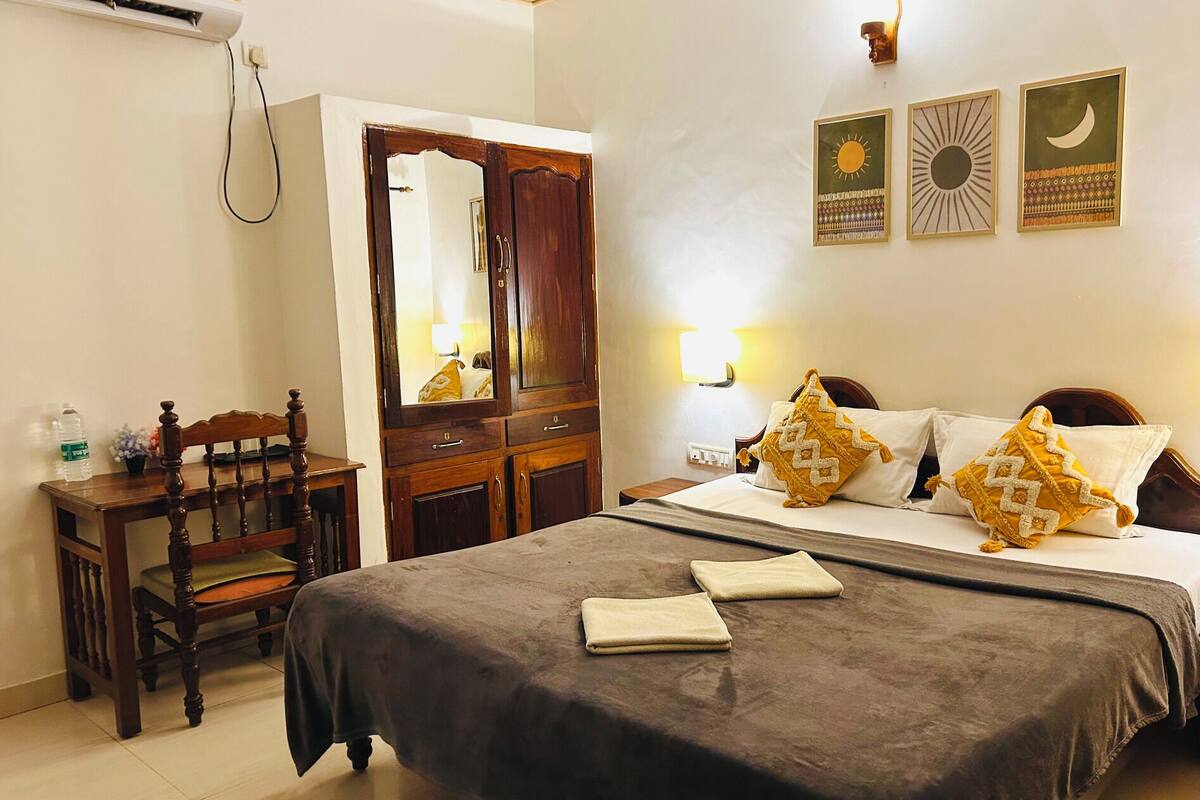 A hotel room with a bed, a wooden chair, a wardrobe, and wall decorations.