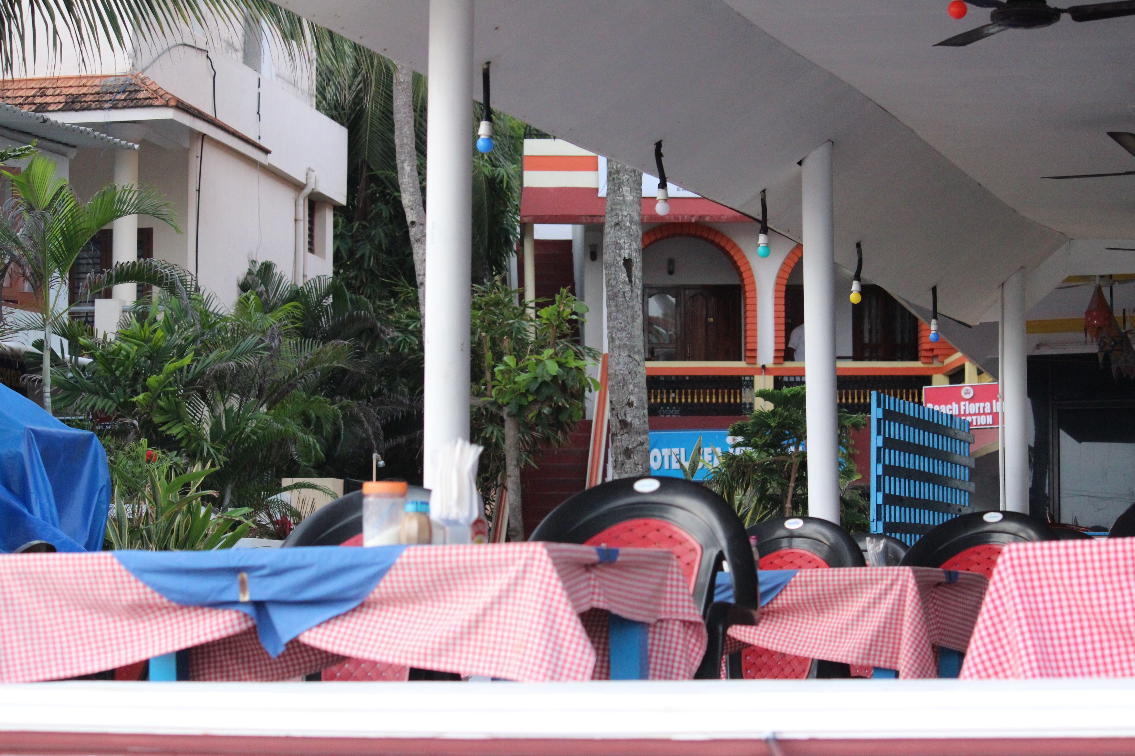 A covered outdoor seating area with tables set up for dining, surrounded by palm trees and a building with a sign that reads "Hotel Florencia."