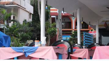 A covered outdoor seating area with tables set up for dining, surrounded by palm trees and a building with a sign that reads "Hotel Florencia."
