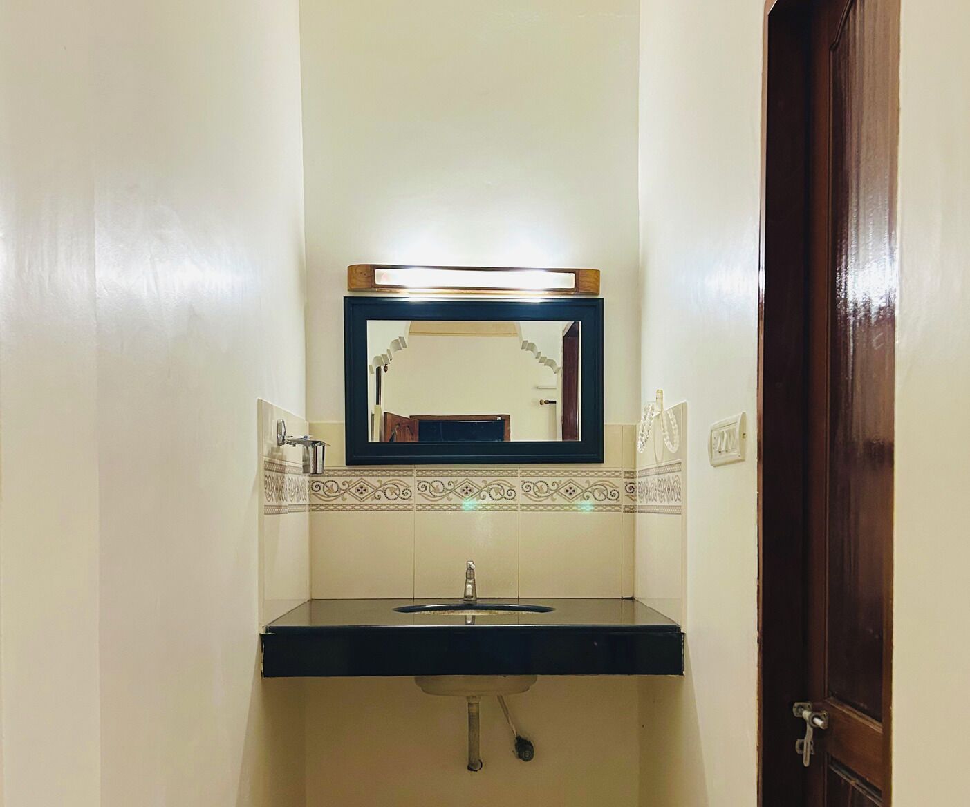 A bathroom with a black sink, a mirror above it, and a decorative tile border.