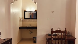 A room with a wooden chair, a small table, a mirror, and an air conditioning unit mounted on the wall.