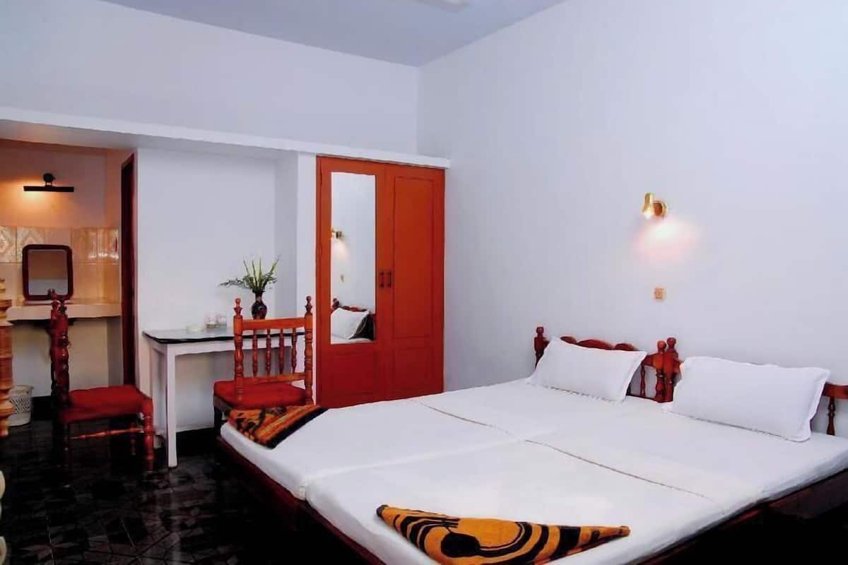 A room with a bed, a desk, a chair, and a red door.