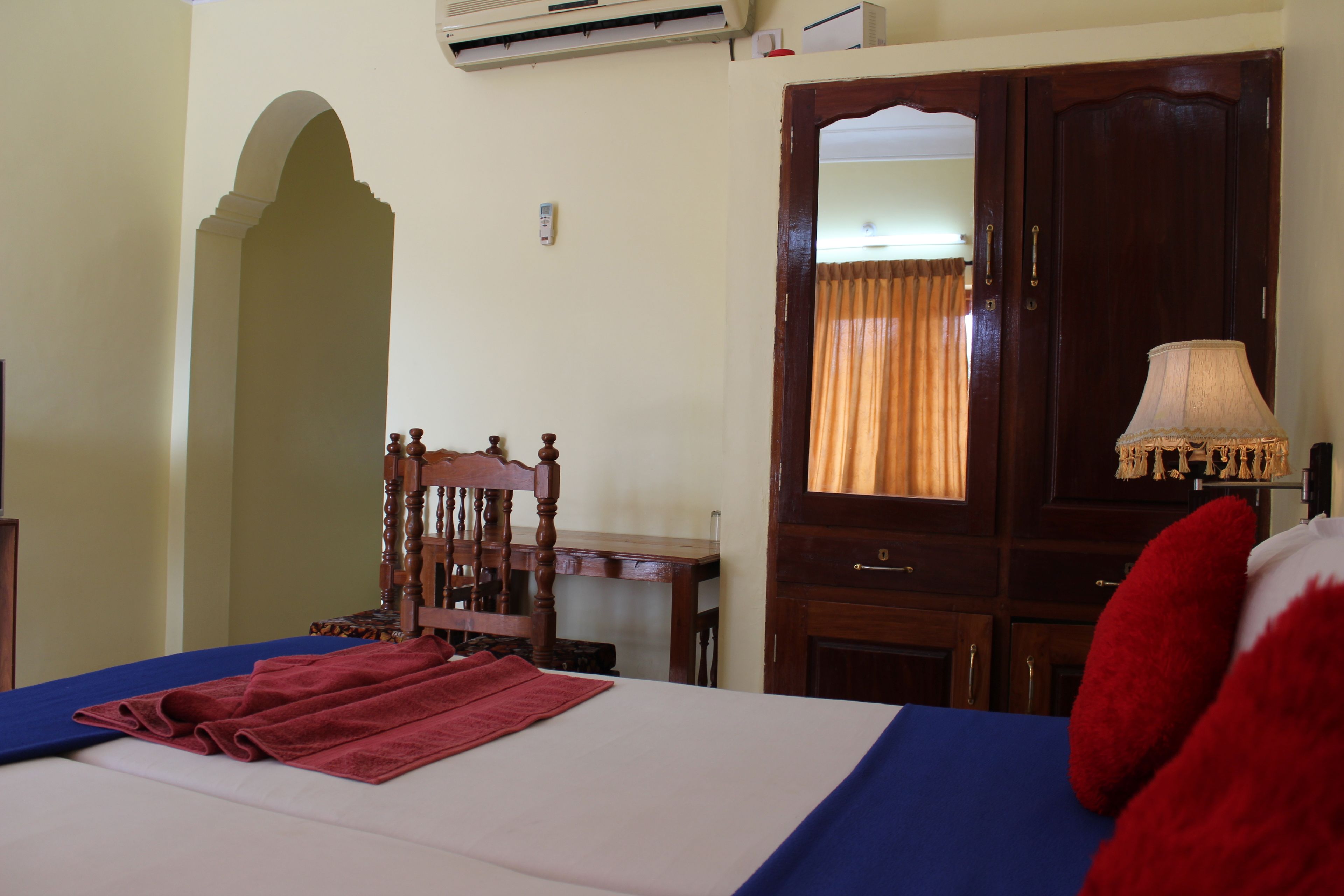 Una habitación de hotel con una cama, una silla de madera, un escritorio, un espejo y una lámpara.