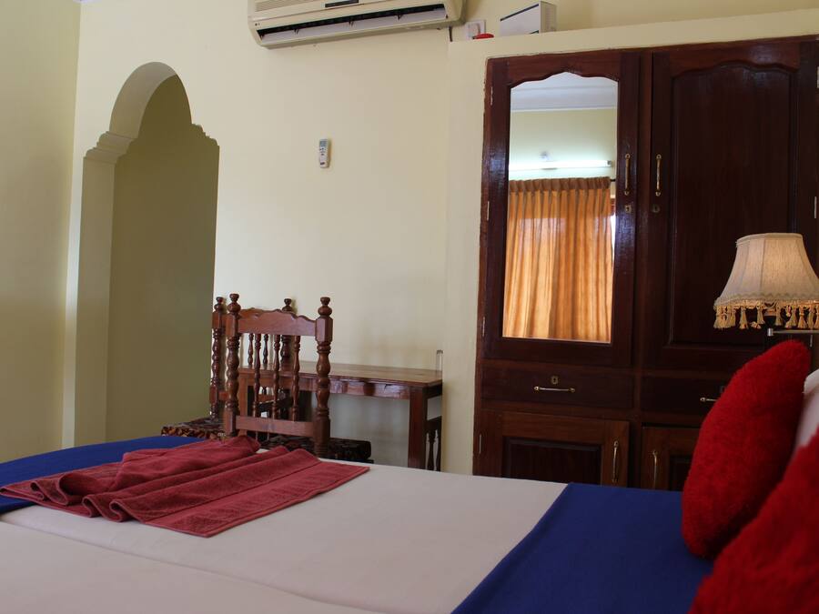 Una habitación de hotel con una cama, una silla de madera, un escritorio, un espejo y una lámpara.