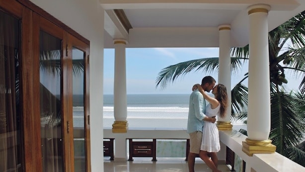 A couple embracing on a balcony with a view of the ocean.