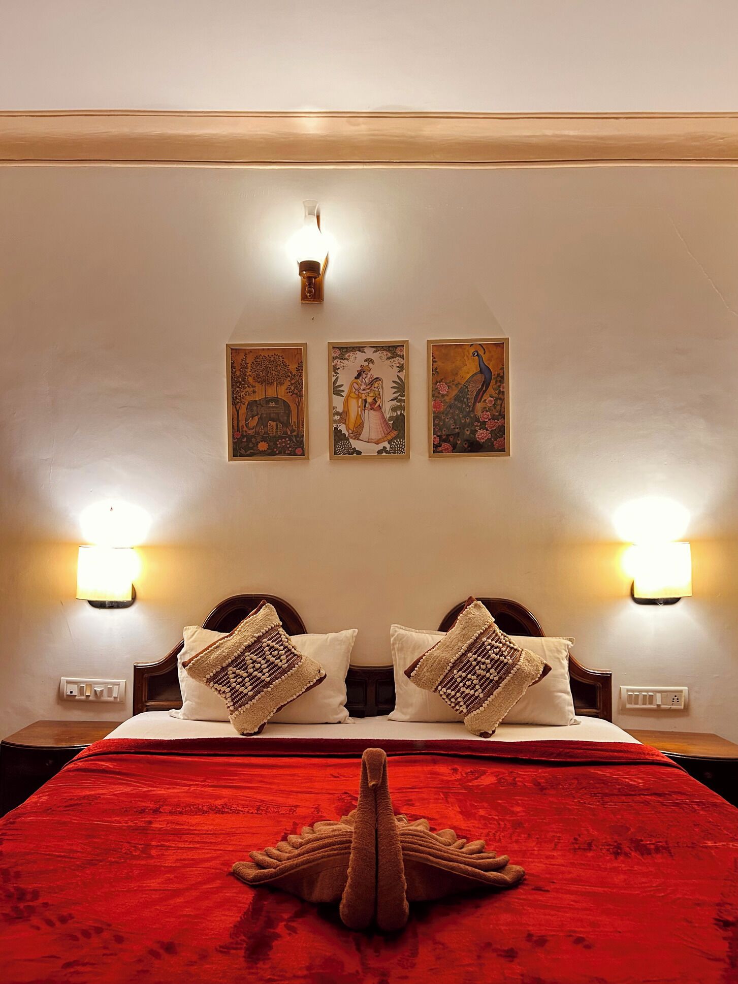 Habitación de hotel con una cama grande, dos lámparas de pared y tres obras de arte enmarcadas en la pared.