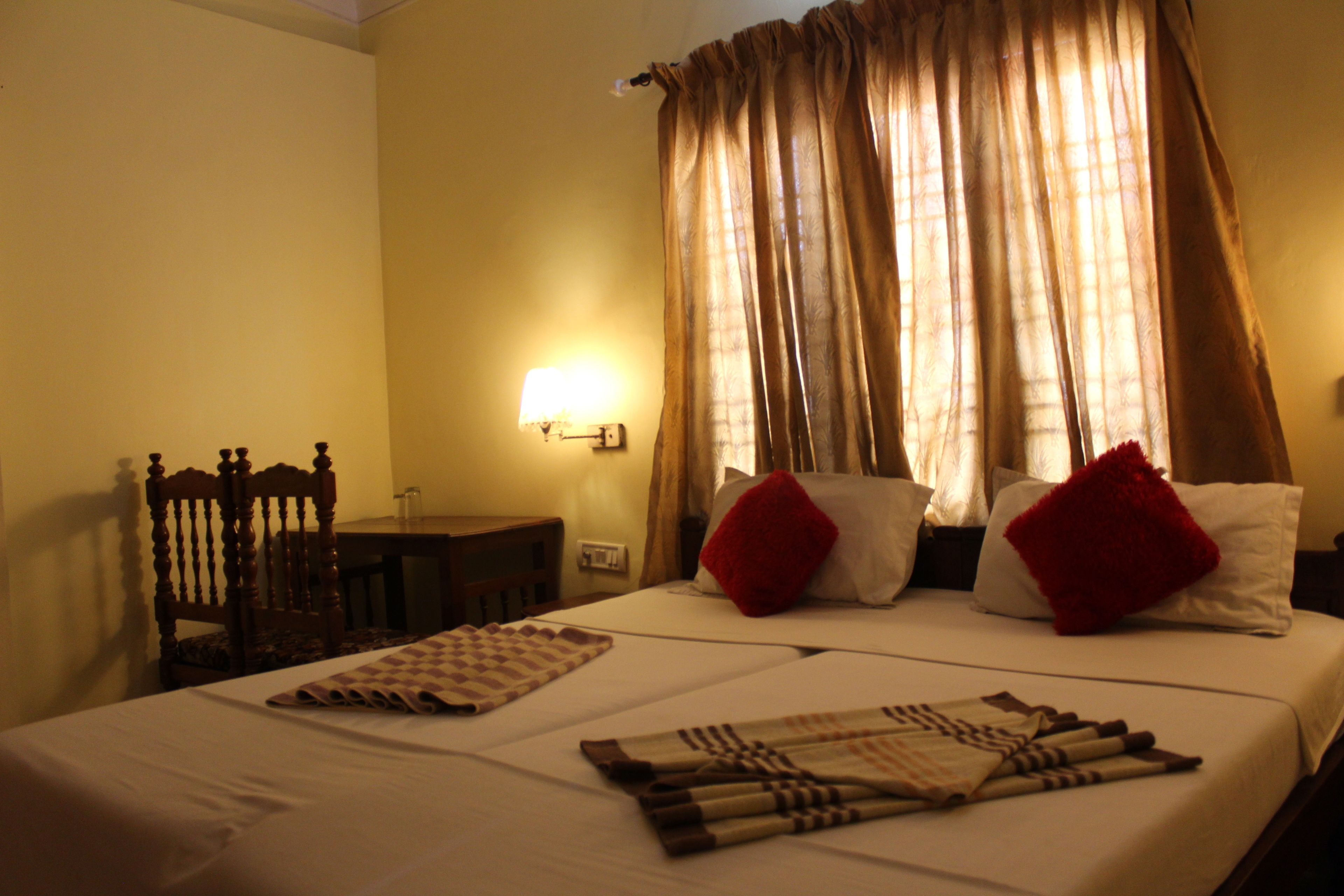 Una habitación de hotel con una cama, una mesita de noche, una lámpara y cortinas.